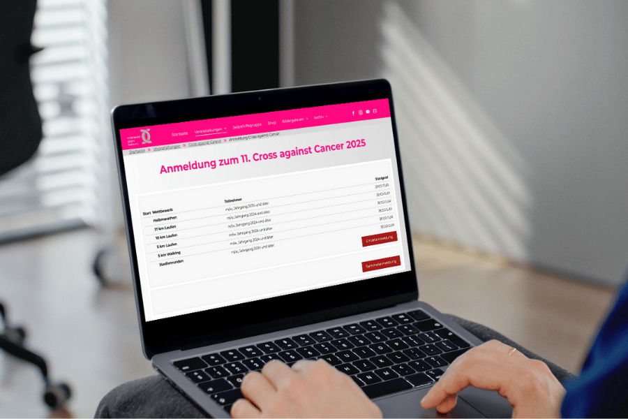 Ein Mensch tippt auf einem Laptop, auf dessen Monitor die Anmeldeseite für den Cross against Cancer geöffnet ist