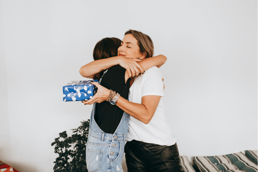 Zwei Frauen umarmen sich, eine hält ein Geschenk in den Händen