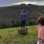 Ein Mädchen steht im Wald mit dem Rücken zur Kamera auf einen Stein