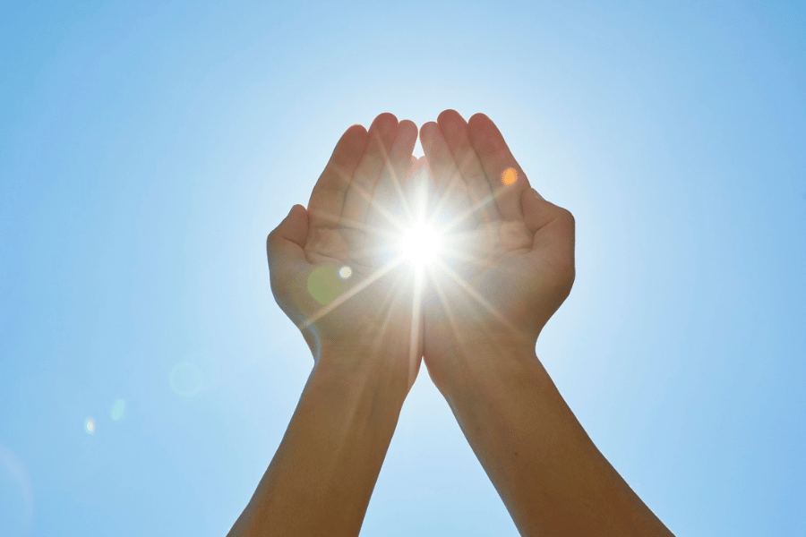 Zwei Hände vor einem blauen Himmel, durch die die Sonne scheint