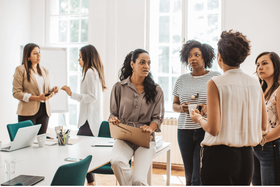 Sechs Frauen stehen in einem Raum und unterhalten sich