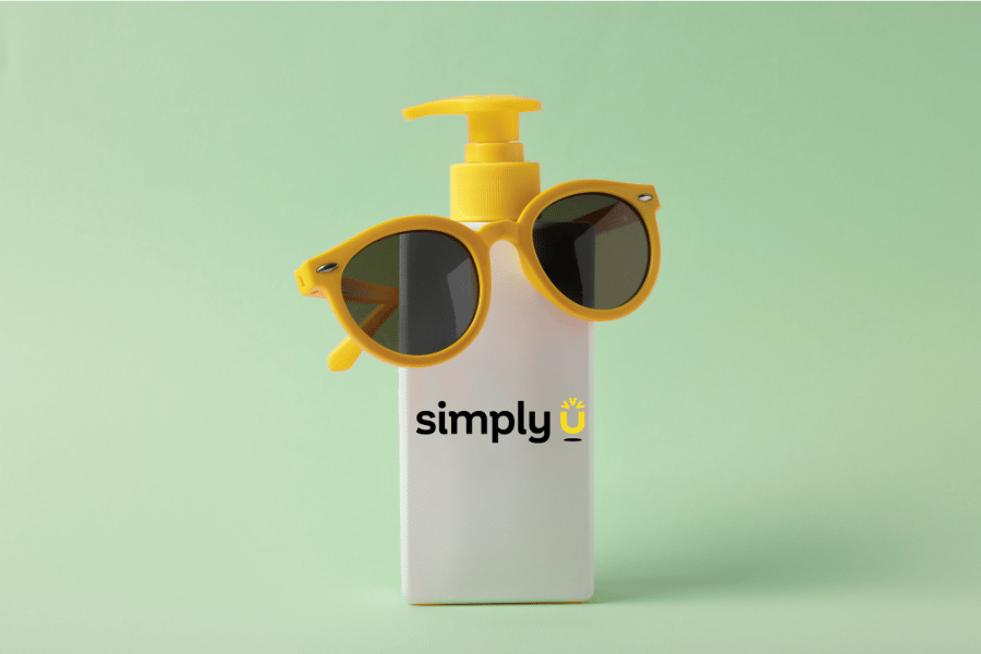 Sonnencreme mit der Aufschrift „Simply U” und eine Sonnenbrille vor einem grünen Hintergrund.