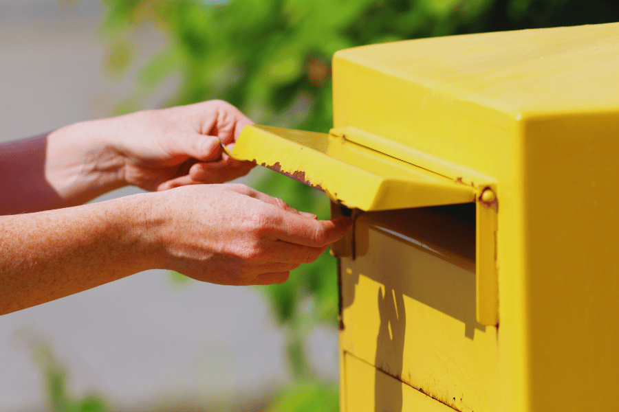 Eine Hand wirft eine Postkarte in einen Briefkasten